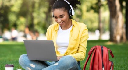 African Student Girl Learning On Laptop Wearing Earphones In Park
